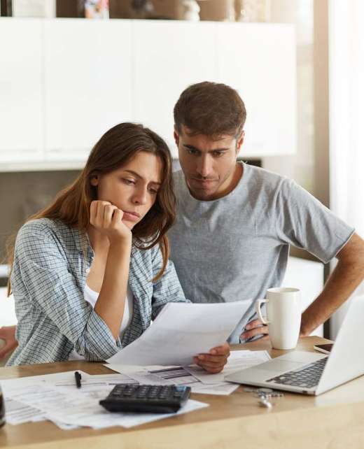 Picture of young wife and husband in kitchen having concentrated looks while reading notification from bank concerning their loan application. Caucasian couple calculating expenses in the morning