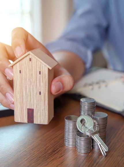 Hand wooden house with key and coins stack in graph shape.